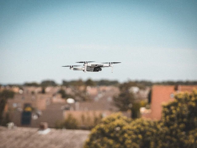 Fliegende Drohne vor einer unscharfen Gebäudekulisse.