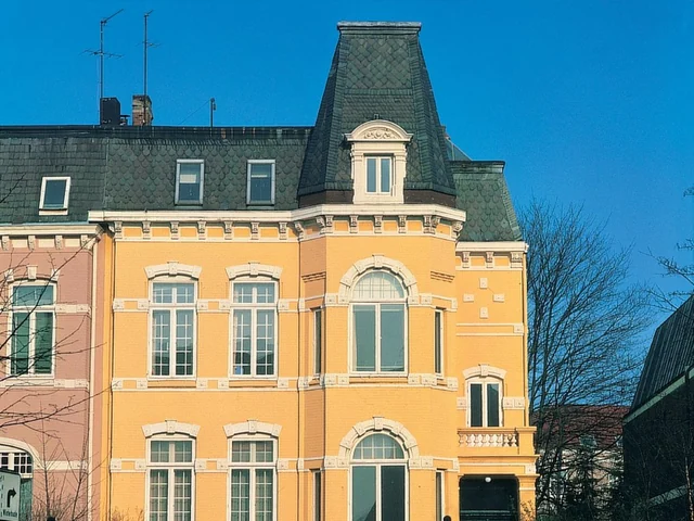Historisches Wohngebäude mit gelber Schmuckfassade und hohem, dunkel gedecktem Dachaufbau.