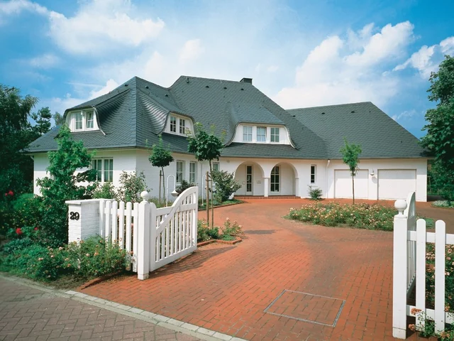 Wohnhaus mit dunklem Schieferdach, mehreren Gauben und weißem Eingangsbereich.