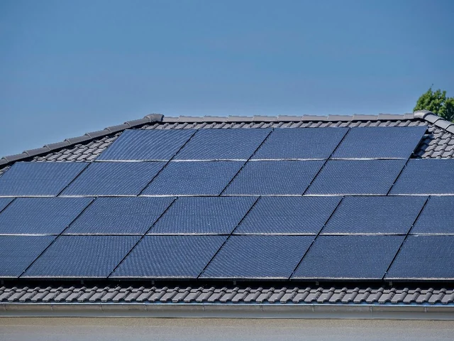 Blaue Solarmodule auf einem dunkel gedeckten Dach vor blauem Himmel.