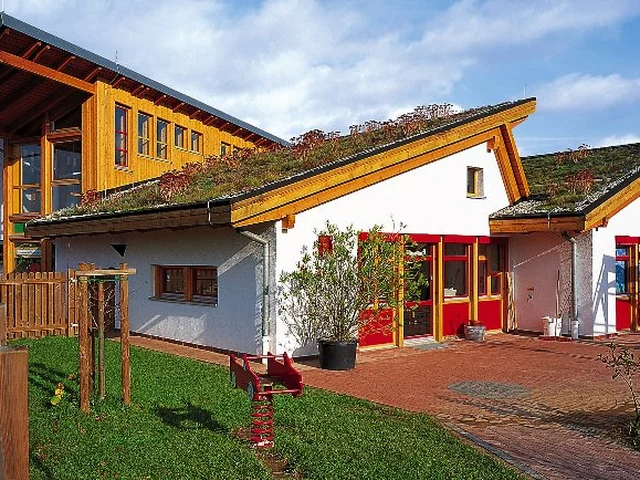 Wohnhaus mit Holzfassade, weißem Anbau und begrünten geneigten Dachflächen.
