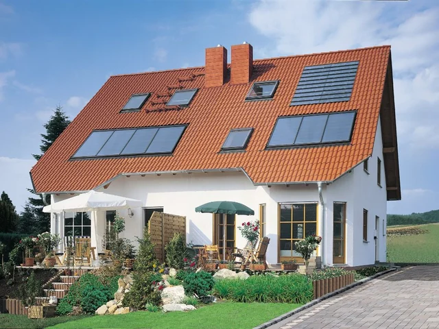 Rotes Ziegeldach mit Dachfenstern und Solarmodulen auf einem weißen Wohnhaus.